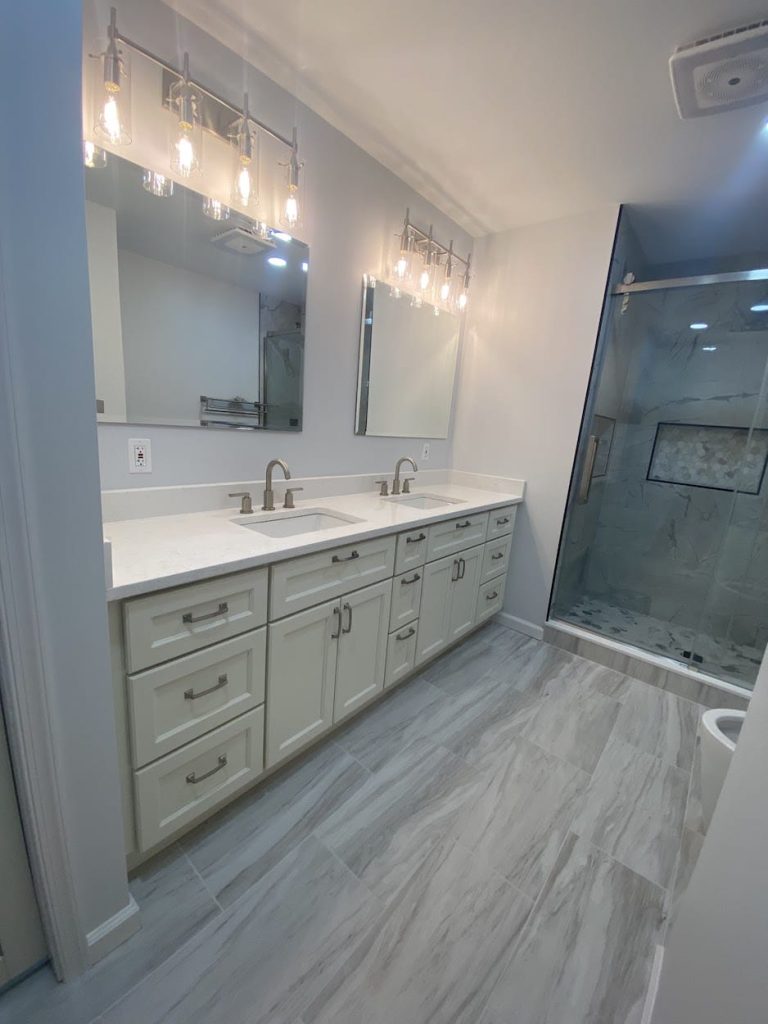 Modern bathroom remodel with double vanity, quartz countertops, lighted mirrors, and walk-in glass shower in PA